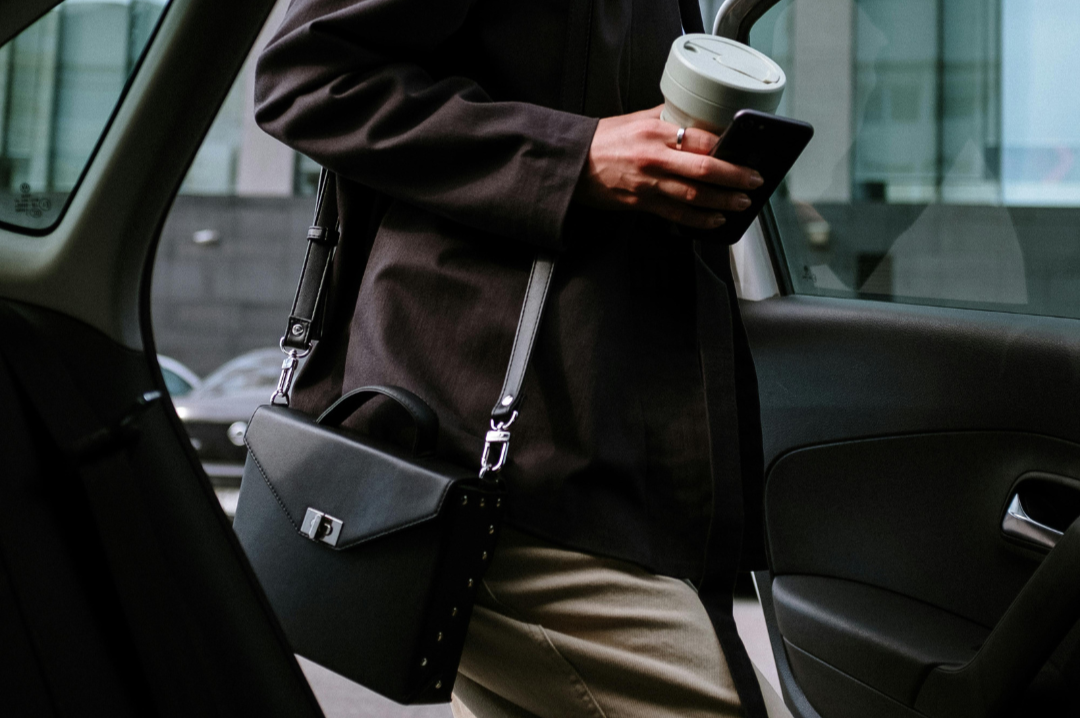 Une femme rentre dans une voiture avec son sac à main et un café